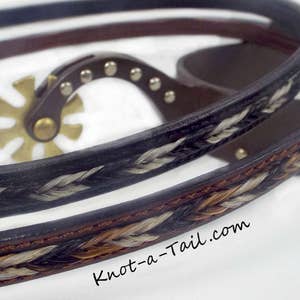 May include: Two leather horsehair braided reins with a silver concho and a horsehair design. The reins are brown and black with white and brown horsehair. The text "Knot-a-Tail.com" is visible on the bottom right.