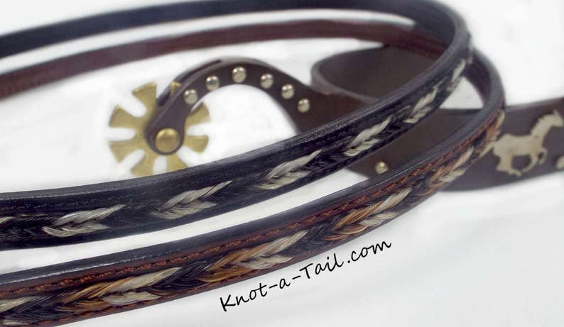 May include: Two leather horsehair braided reins with a silver concho and a horsehair design. The reins are brown and black with white and brown horsehair. The text "Knot-a-Tail.com" is visible on the bottom right.