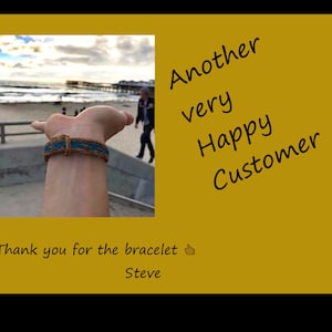 Puede incluir: Una persona lleva una pulsera trenzada azul y marr&oacute;n con una escena de playa en el fondo. El texto "Another very Happy Customer" y "Thank you for the bracelet 👍 Steve" es visible en la imagen.