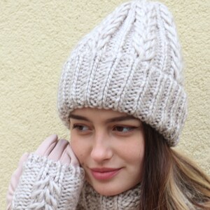 May include: A woman wearing a beige knitted hat, matching gloves, and a scarf. The hat, gloves, and scarf all have a cable knit pattern.