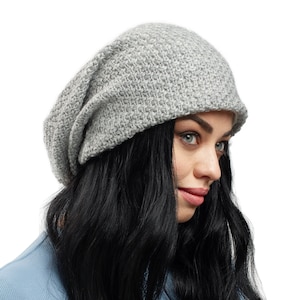 Op de afbeelding: Een grijze slouchy beanie met een textuur geweven patroon. De muts wordt gedragen door een persoon met lang zwart haar.