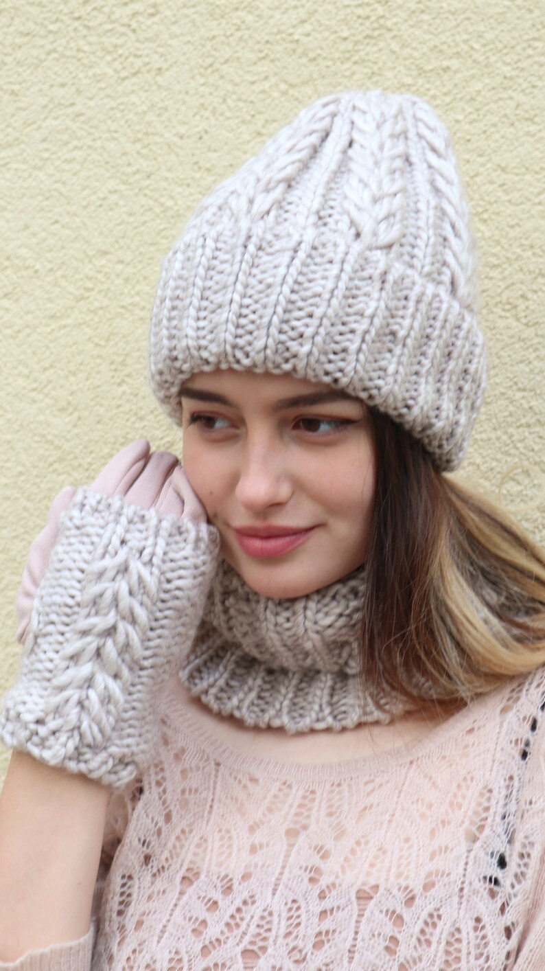 May include: A woman wearing a beige knitted hat, matching gloves, and a scarf. The hat, gloves, and scarf all have a cable knit pattern.