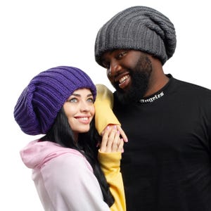 May include: A dark gray ribbed knit beanie and a vibrant purple ribbed knit beanie. The dark gray beanie is worn by a person in a black shirt with the text Angeles printed on the collar. The purple beanie is worn by a person in a pink hoodie.