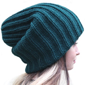 Puede incluir: Un gorro de punto verde oscuro con un ajuste holgado. El gorro está hecho de un hilo grueso y suave y tiene una textura acanalada.