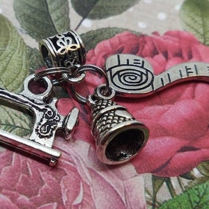 May include: Silver charm set featuring a sewing machine, thimble, and a measuring tape. The charms are attached to a silver chain.
