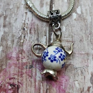May include: A silver charm bracelet with a blue and white teapot charm. The teapot has a floral design.
