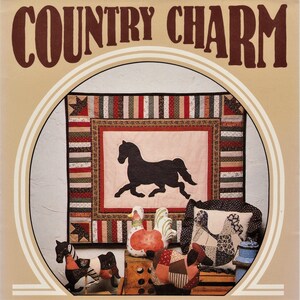 May include: A quilt pattern book titled "Country Charm" featuring a black silhouette of a horse on a patchwork quilt with a red, white and green border. The quilt is surrounded by handmade fabric toys, including a rocking horse, a rooster and a hen.