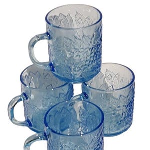 May include: Set of four blue glass mugs with a grapevine design. The mugs are stacked on top of each other.