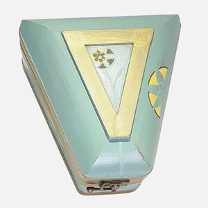 May include: A triangular, hinged box in a light blue hue, accented with gold trim. The box features a gold triangle on the lid, framing a floral design. A small, ornate clasp secures the box, suggesting it's for jewelry or small keepsakes.