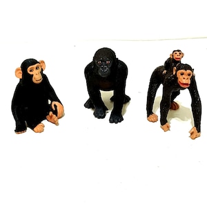 May include: Three black plastic toy chimpanzees. One chimpanzee is sitting with its legs crossed. Another chimpanzee is standing with its arms raised. The third chimpanzee is standing with its arms at its sides.
