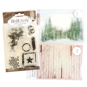Peut inclure: Tampons transparents pour le scrapbooking, avec diverses textures et motifs. Comprend un ensemble de tampons avec un arbre, des cercles, une étoile et d'autres formes. Comprend également des tampons d'une scène de forêt et d'un motif de planches de bois. L'emballage indique "BoBunny Terrific Textures Stamps."