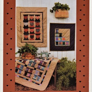May include: Three quilted wall hangings with a patchwork design featuring a variety of colors and patterns, including red, blue, green, and brown. The hangings are displayed on a white wall with a wooden table in the foreground. The table is covered with a quilt with a similar patchwork design.