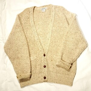 May include: A cream-colored knitted cardigan with a V-neck and button closure. The cardigan has a speckled pattern and two pockets.