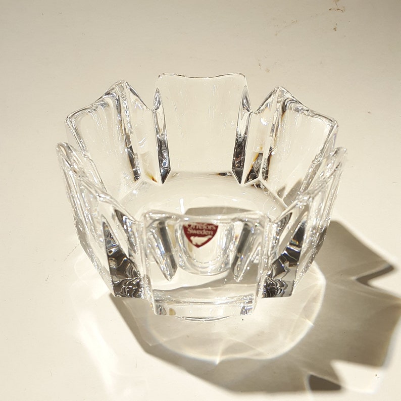May include: A clear glass bowl with a faceted design. The bowl has a starburst shape and is made by Orrefors Sweden.