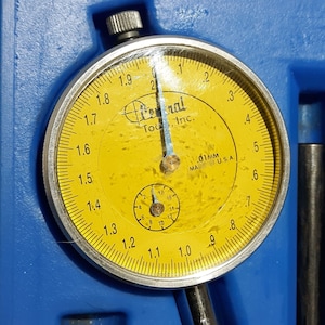 May include: A yellow dial gauge with a black needle and a silver rim. The gauge reads from 0.8 to 2.0 in increments of 0.1. The gauge is labeled "Central Tool, Inc." and "0.01mm Made in U.S.A."