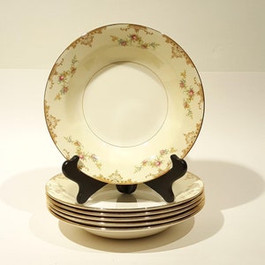 Puede incluir: Un juego de seis cuencos de sopa de porcelana blanca vintage con borde dorado y estampado floral. Los cuencos están apilados en un soporte negro.