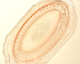 Pode incluir: Um prato oval de servir de vidro rosa com um design floral em relevo. O prato tem uma borda festonada e um padrão de nervuras ao redor do centro.
