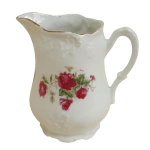 May include: White porcelain creamer with a floral design featuring pink roses and green leaves. The creamer has a scalloped rim and a gold trim.