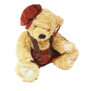 May include: A plush teddy bear wearing a red corduroy hat and overalls. The bear has a brown nose and black eyes.