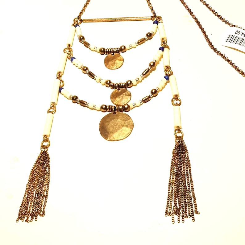 May include: A gold necklace with three layers of white and blue beads, three gold coin pendants, and two gold tassel charms.