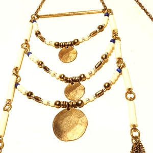 May include: A gold necklace with three layers of white and blue beads, and three gold circular pendants. The necklace has a gold bar at the top.
