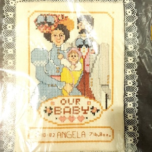 Könnte beinhalten: Stickmuster mit einer dreiköpfigen Familie mit dem Text "Our Baby" und dem Datum "10-82 ANGELA 7lb.8oz."