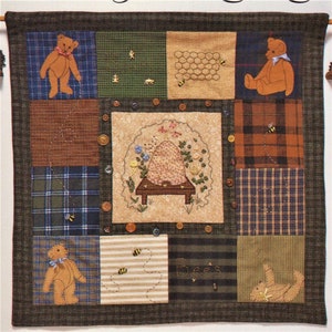 Puede incluir: Una colcha de retazos marrón y beige con un tema de colmena. La colcha presenta abejas bordadas, panales y osos de peluche. La colcha está hecha de diferentes telas, incluyendo cuadros, rayas y colores sólidos. La colcha está colgada en una pared.