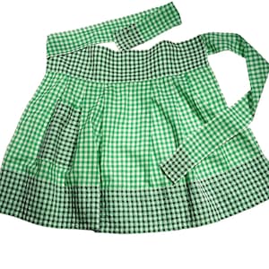May include: A green and white checkered apron with black checkered accents. The apron has a pocket and a waistband with long ties. The apron is made of fabric and is designed for kitchen use.