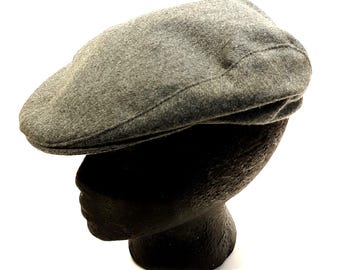 May include: A solid grey flat cap featuring a rounded crown and a short, stiffened brim. The hat is constructed from a textured fabric with visible stitching along the seams, displaying a classic low-profile silhouette that sits flat against the head.