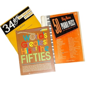 Könnte beinhalten: Drei Vintage-Notenbücher. Die Einbände sind gelb, orange und braun. Das gelbe Buch trägt die Aufschrift "34 More Hit Parade Extras". Das braune Buch trägt die Aufschrift "World's Greatest Hits of the Fifties". Das orangefarbene Buch trägt die Aufschrift "50 Big Note Piano Pieces."