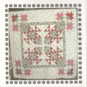 May include: A square quilt with a floral pattern background and a central design of red and white triangles. Red star shapes are in each corner. The quilt is framed with a black and white floral border.
