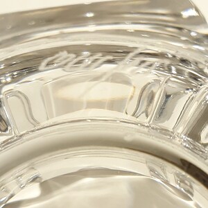 May include: Close-up of the base of a clear glass goblet with the inscription "Cristal d'Arques" etched into the glass.