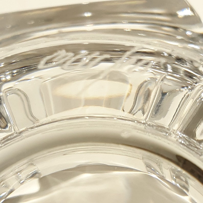 May include: Close-up of the base of a clear glass goblet with the inscription "Cristal d'Arques" etched into the glass.