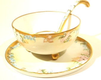 May include: A vintage porcelain serving bowl with a matching saucer and a gold-trimmed spoon. The bowl and saucer feature a floral design with pink roses and blue forget-me-nots.