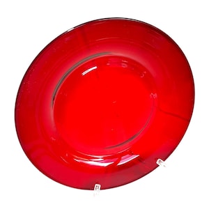 May include: A vibrant red glass plate with a glossy finish. The plate has a wide, flat rim and a slightly recessed center. The color is a deep, saturated red, and the plate appears to be made of a single piece of glass.