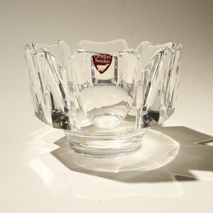 May include: A clear glass bowl with a scalloped edge and a starburst pattern. The bowl has a small, red label that reads "Orrefors Sweden".