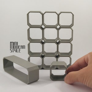 May include: A set of gray geometric shelves made of plastic. The shelves are arranged in a grid pattern and are designed to be stacked on top of each other. The shelves are small and would be suitable for displaying small items.