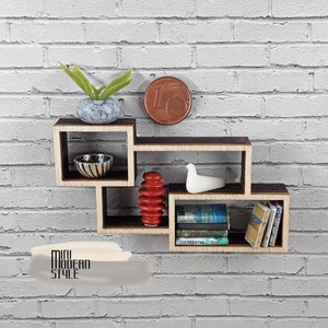 Può includere: Un'unità a mensola in legno in miniatura con un design moderno. La mensola ha tre livelli ed è decorata con una piccola pianta in vaso, una ciotola, una pila di blocchi rossi, una statuetta di uccello bianca e una fila di libri. La mensola è montata su un muro di mattoni bianchi.