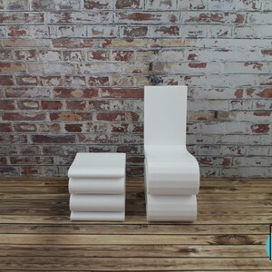 Puede incluir: Silla y mesa auxiliar blancas modernas con un dise&ntilde;o curvo. La silla y la mesa est&aacute;n frente a una pared de ladrillo y un suelo de madera.