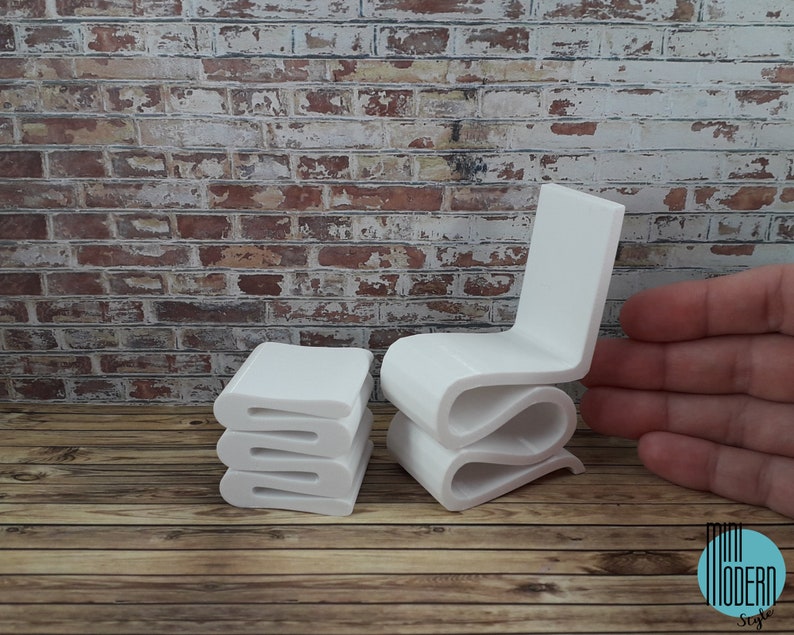 Puede incluir: Conjunto de silla y otomana en miniatura de color blanco. La silla y la otomana est&aacute;n hechas de un material blanco liso y tienen un dise&ntilde;o moderno y abstracto. La silla tiene un respaldo y un asiento curvos, y la otomana es una pila de tres piezas rectangulares.