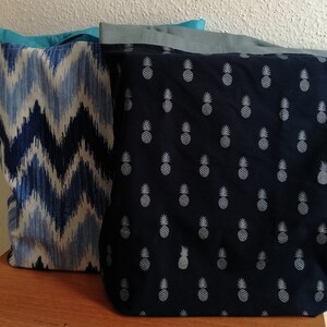 Puede incluir: Dos bolsas de tela. Una bolsa presenta un patrón de zigzag azul y blanco, y la otra tiene un fondo azul marino con un estampado de piñas blancas. Ambas bolsas tienen forros de colores contrastantes.