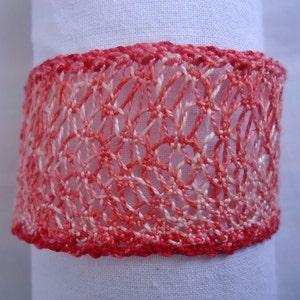 May include: A close-up of a red and white crocheted lace trim. The trim is made of a delicate, openwork design and has a slightly ombre effect, fading from a darker red to a lighter white.