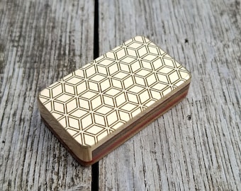 May include: A small, rectangular box made of wood with a geometric pattern on the top. The box is made of multiple layers of wood, with a red, brown, and white colour scheme. The box has a gold-coloured geometric pattern on the top.