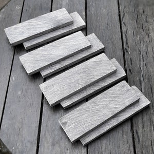 May include: A set of five grey rectangular sharpening stones stacked on top of each other on a wooden surface.