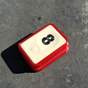 May include: A red and white plastic tile with the number 8 printed in black. The tile has a small circle with the word "WIN" printed inside.