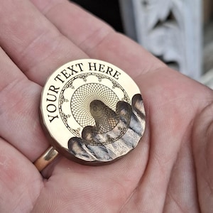 May include: A gold-coloured metal stamp with the text "YOUR TEXT HERE" engraved around the edge. The centre of the stamp features a detailed design of a Ferris wheel.
