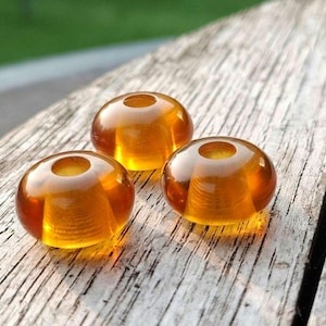 May include: Three amber glass beads with a hole in the center. The beads are round and have a smooth, glossy finish.