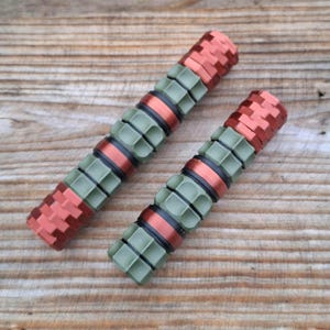 May include: Two cylindrical metal objects featuring a repeating pattern of alternating matte olive green textured segments and smooth metallic copper-coloured bands. The design includes black O-ring spacers between the sections, creating a modular look.