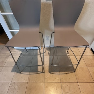 May include: Two gray bar stools with chrome legs. The stools are on a tiled floor.