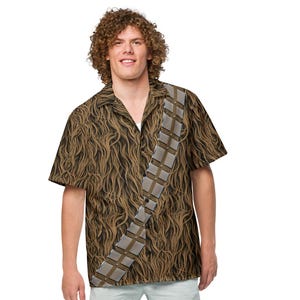 May include: A brown and tan short-sleeve button-down shirt with a pattern resembling fur, featuring a gray bandolier design. The person is wearing light blue shorts and white sneakers.